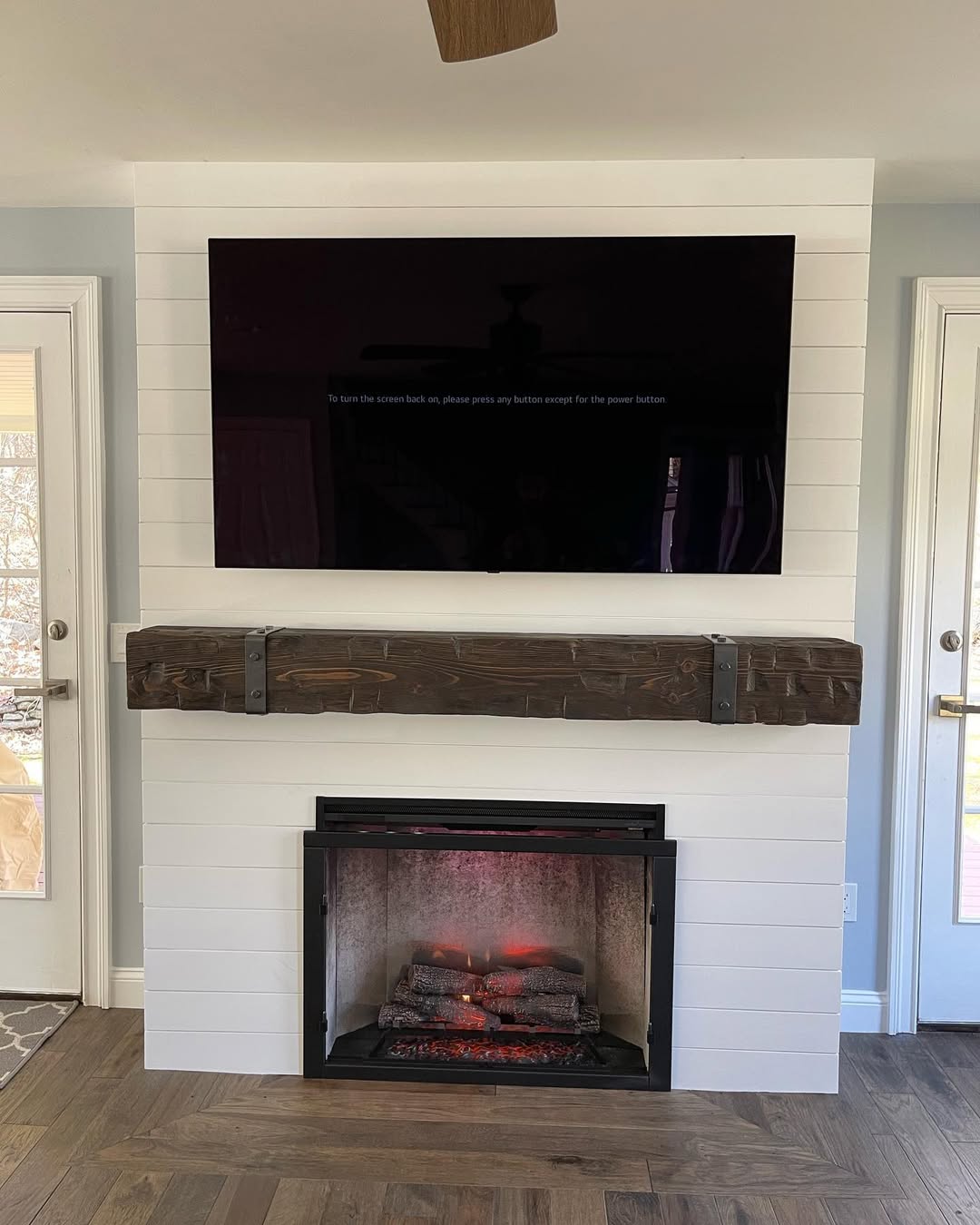 Shiplap fireplace feature wall with a rough-hewn timber mantel on iron brackets and a mounted television