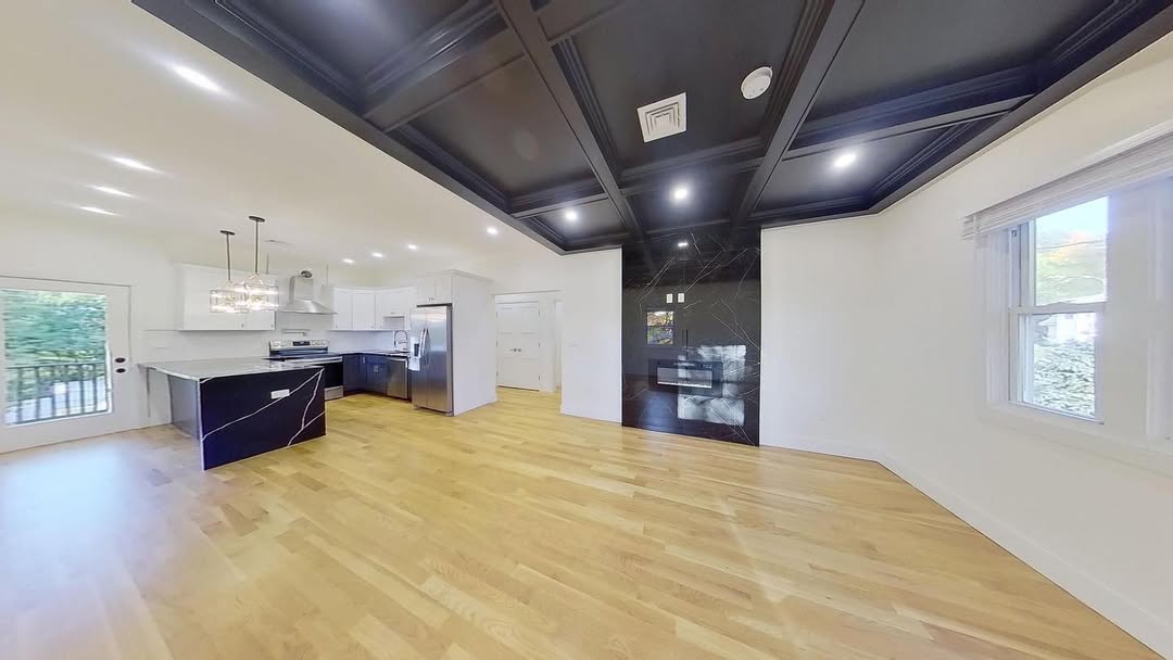 Open living space with a black coffered ceiling above white oak flooring and an open kitchen